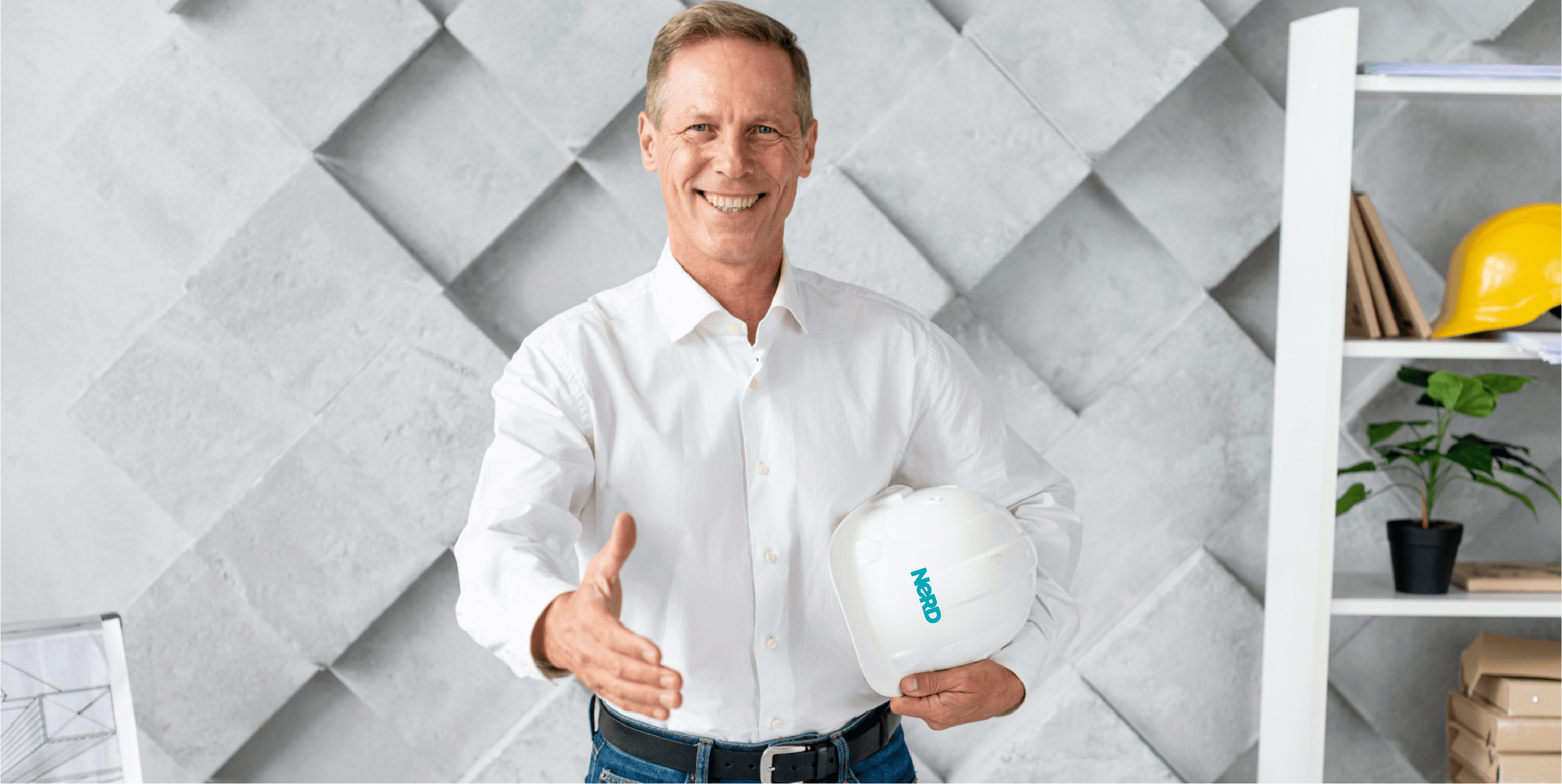A sharply dressed man inside a home, holding out his right arm to shake hands, and carrying a white hard hat under his left arm.